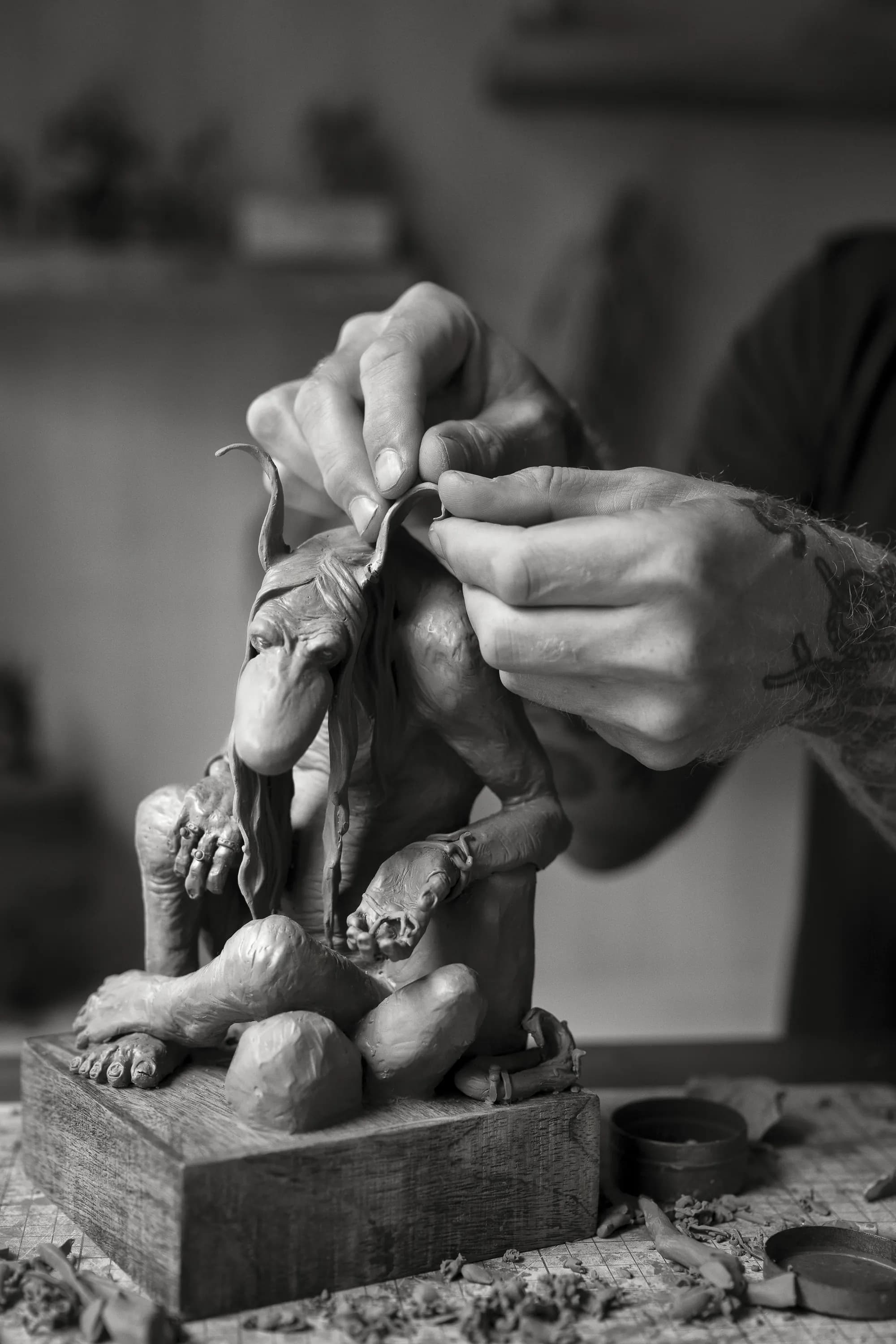 Hands shaping the ear of a clay troll sculpture on a workbench